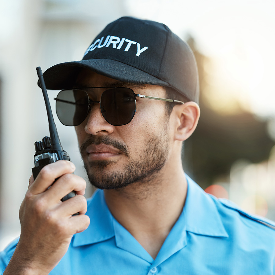 A security officer in uniform holds a walkie talkie, ready to communicate and ensure safety.